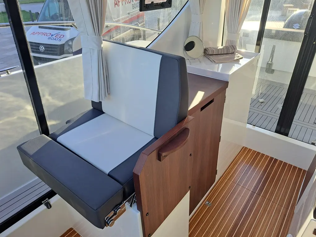 Interior view of a boat featuring a grey and white upholstered seat, wooden cabinetry, and a striped wooden floor.